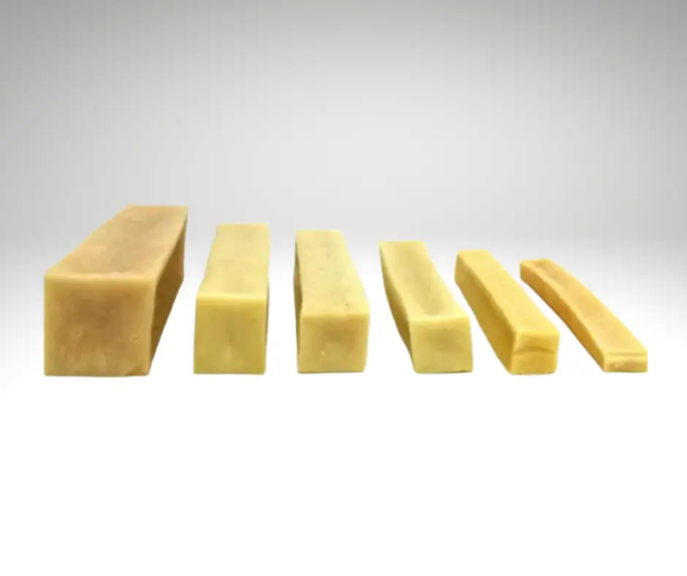 Bâtons de fromage de yak Cheezy-Dog de tailles différentes alignés sur un fond gris clair.